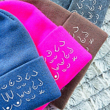Load image into Gallery viewer, Three beanies in blue, pink, and brown with white text on a textured surface.