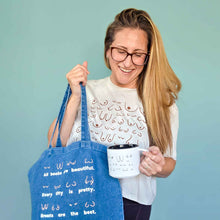 Load image into Gallery viewer, Woman holding a blue tote bag and a white mug with text against a light blue background