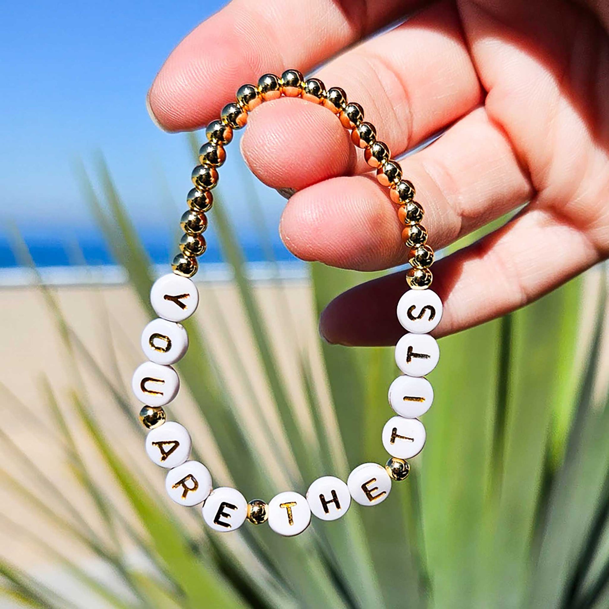 Bracelet with motivational message held by a hand against a beach background