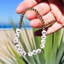 Load image into Gallery viewer, Bracelet with motivational message held by a hand against a beach background
