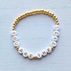 Bracelet with white beads and gold accents on a light textured background