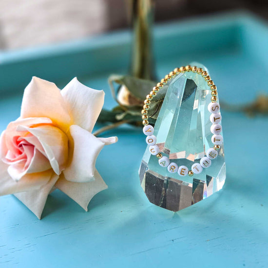 Crystal decoration with bracelet with text next to a pink flower on a blue surface