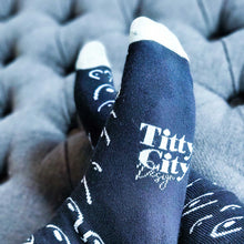 Load image into Gallery viewer, Black socks with white text and patterns on a gray ottoman
