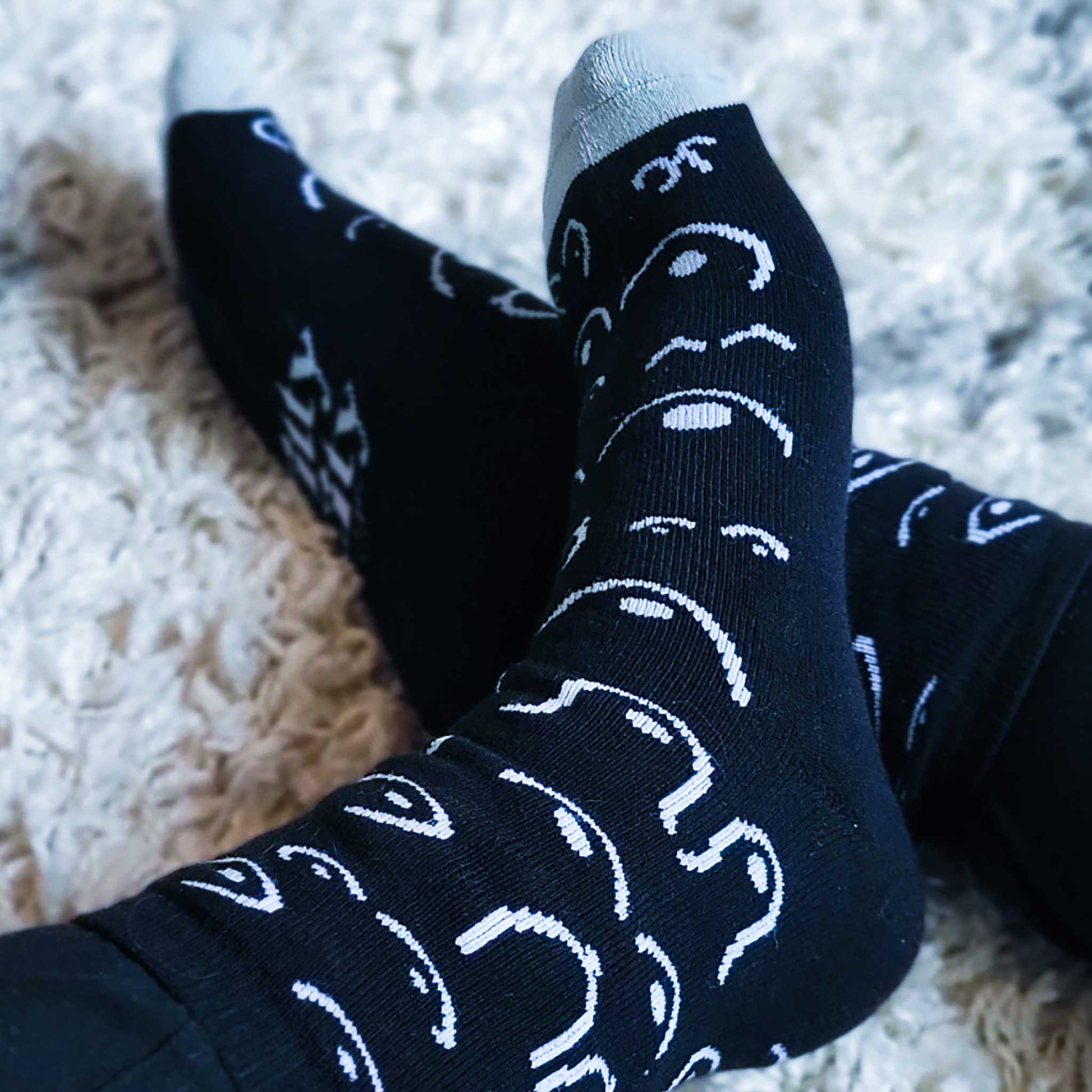 Black socks with white patterns worn on a light carpet