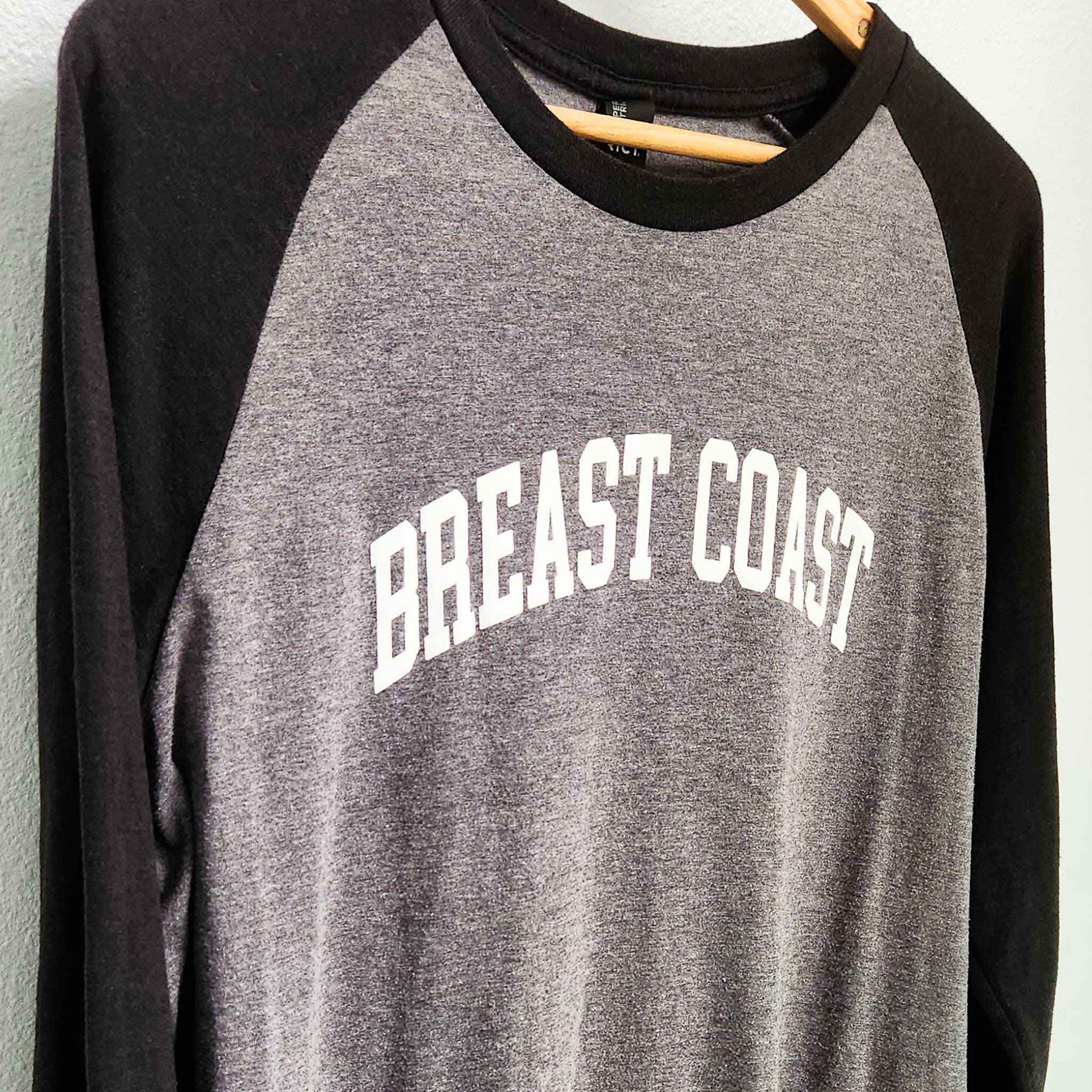 Breast Coast baseball t-shirt with gray body and black sleeves with slogan across the chest, close up, front view, on hanger
