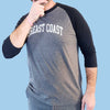 Model wearing Breast Coast baseball t-shirt with gray body and black sleeves with slogan across the chest, front view