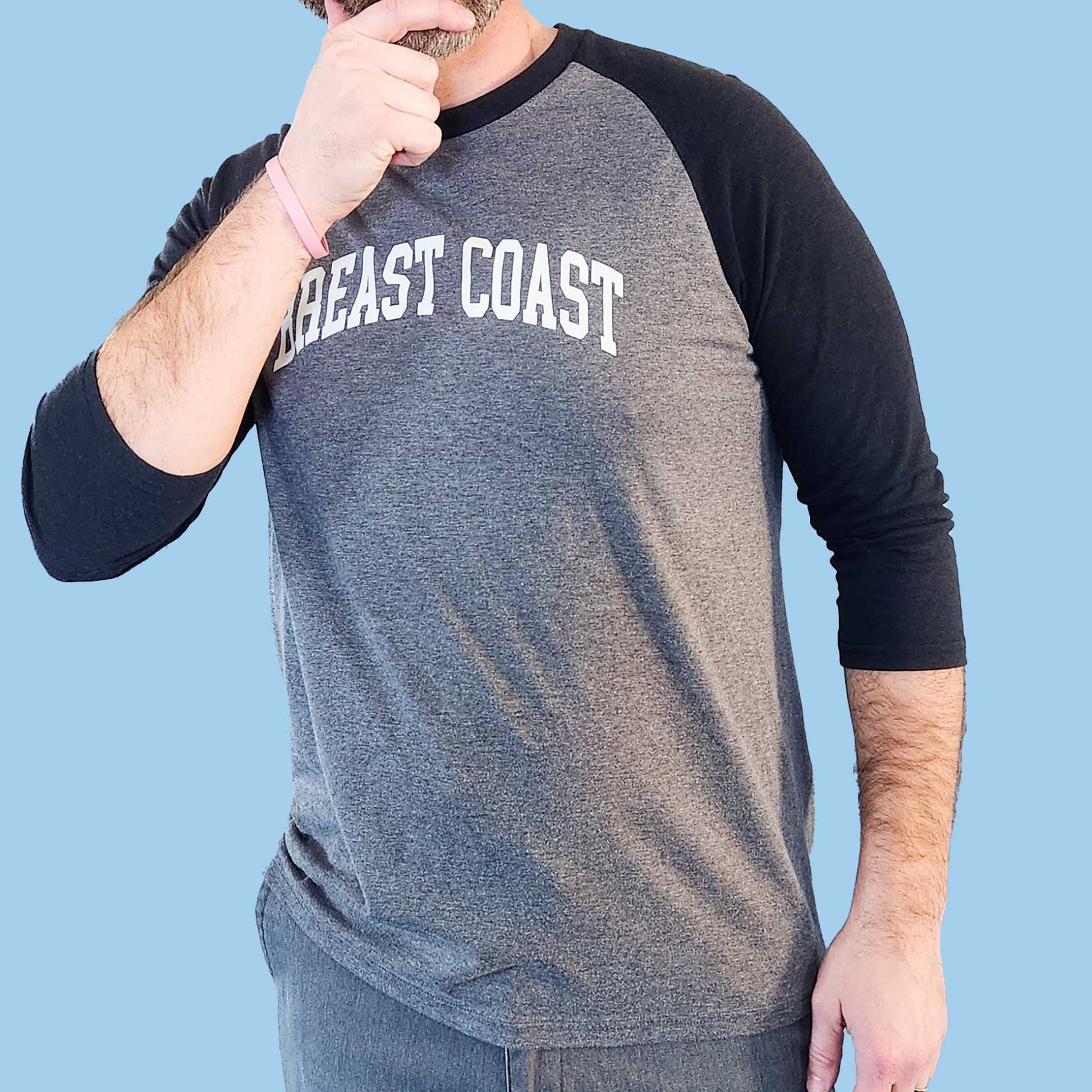 Model wearing Breast Coast baseball t-shirt with gray body and black sleeves with slogan across the chest, front view