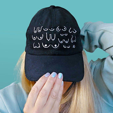 Black cotton corduroy dad cap with white patterns worn by a person against a teal background