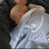 Baby wrapped in a gray blanket with white patterns, being held by an adult.