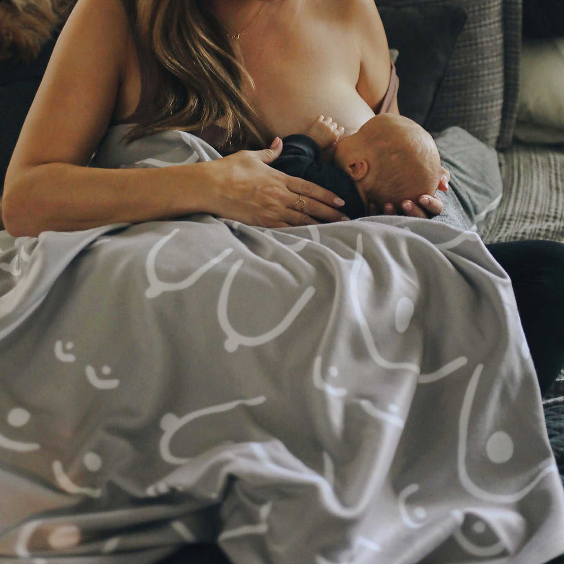 Woman breastfeeding a baby on a couch with a blanket that has patterns.