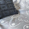Gray textured pillow on a gray fabric surface with white patterns