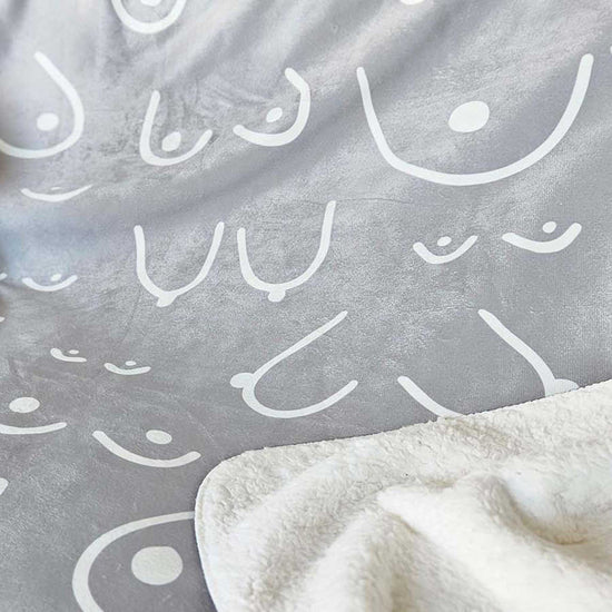 Gray blanket with white abstract patterns and a corner of a white blanket.
