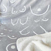 Gray blanket with white abstract patterns and a corner of a white blanket.