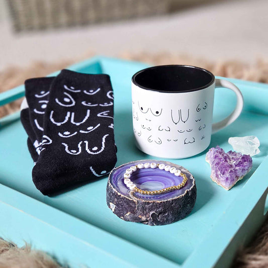 Black socks with white patterns, a white mug with black interior, and a purple crystal on a turquoise tray.