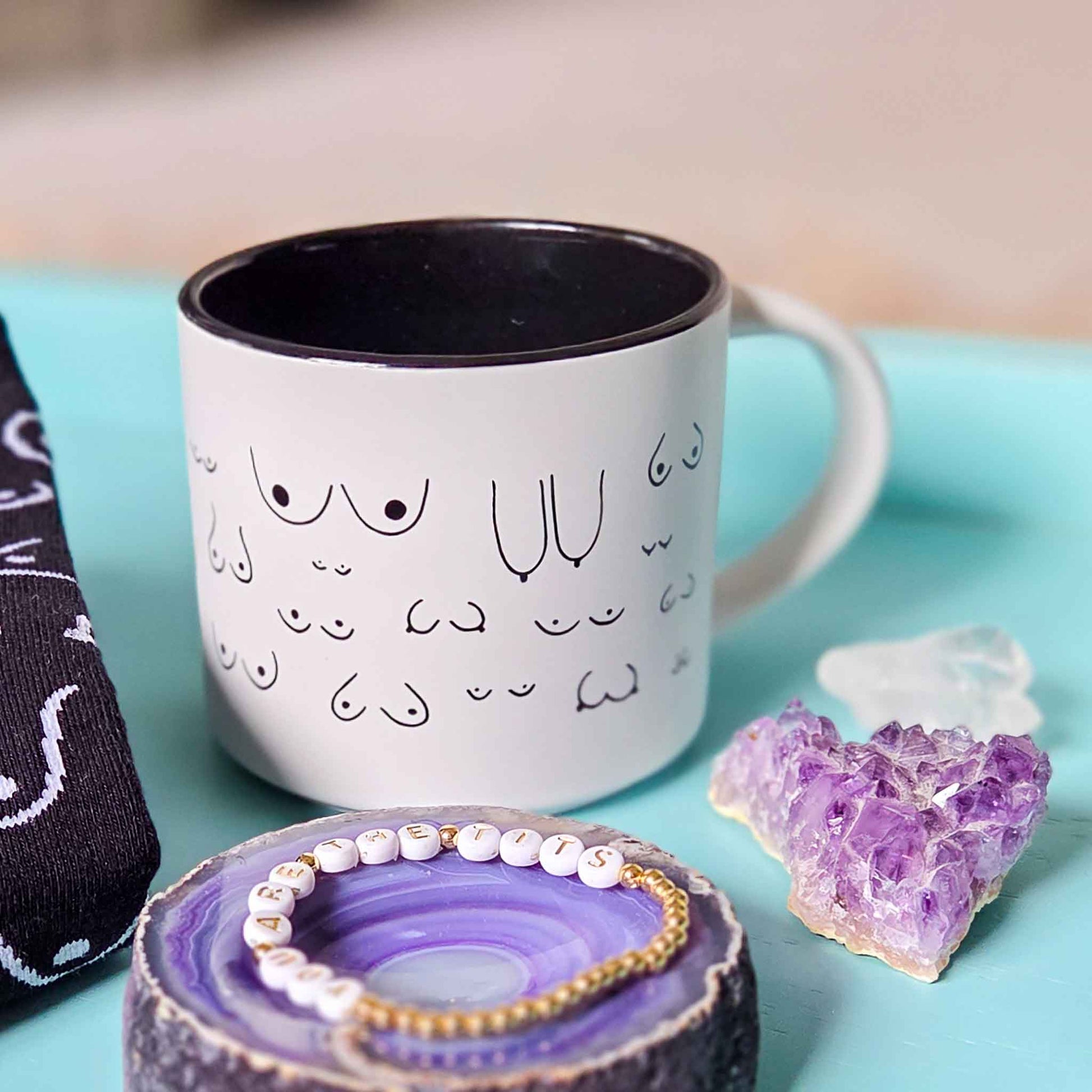 White mug with black designs on a blue surface with jewelry and crystals.