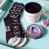 Black socks with white patterns, a white mug with black interior, and a purple decorative item on a light blue surface.