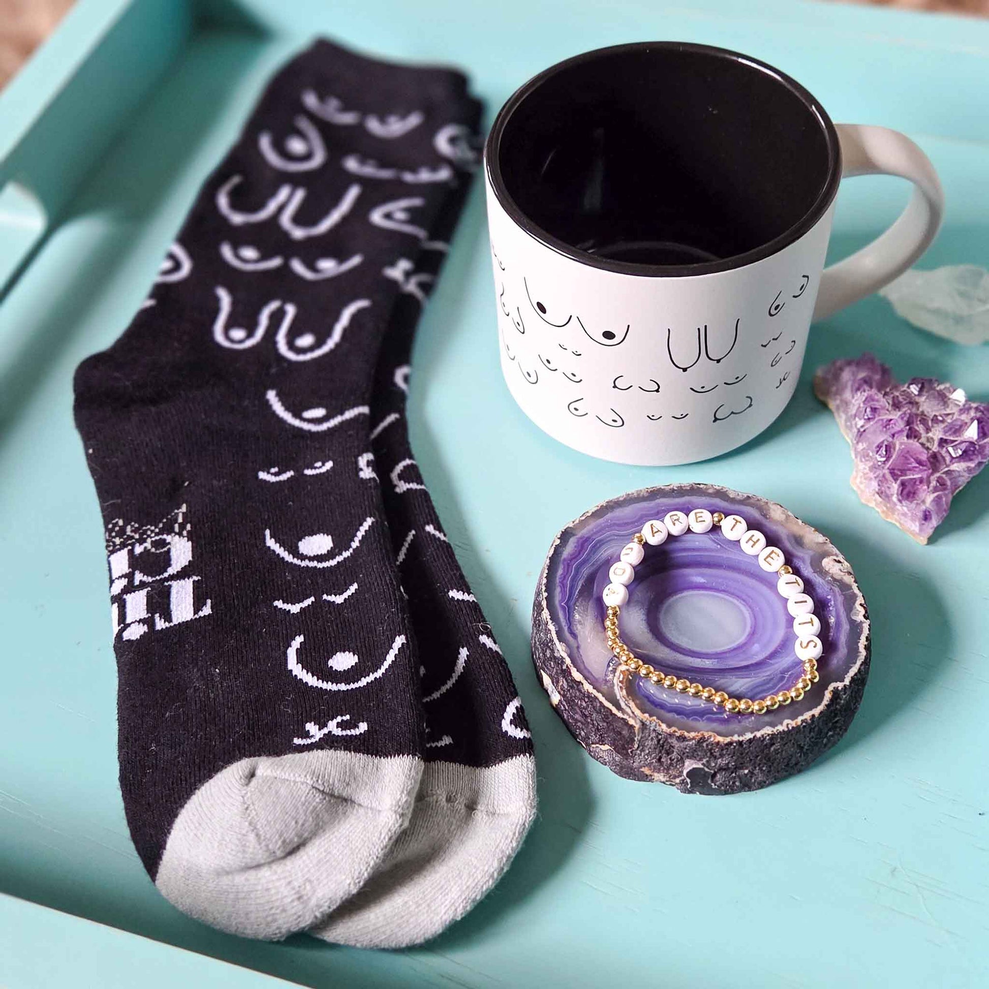 Black socks with white patterns, a white mug with black interior, and a purple decorative item on a light blue surface.