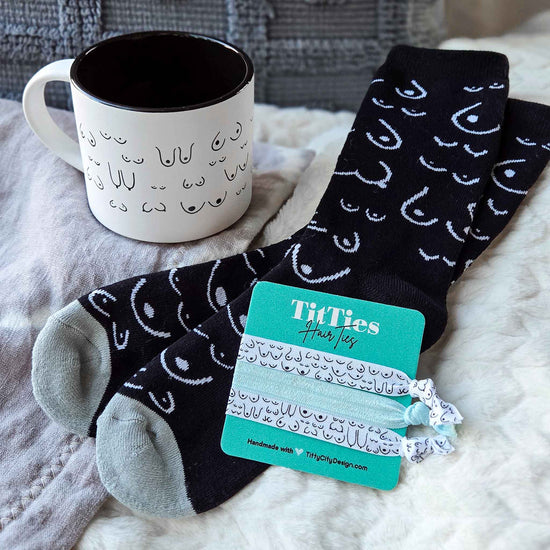 Pair of black socks with white patterns, a mug, and a hair tie on a textured surface.