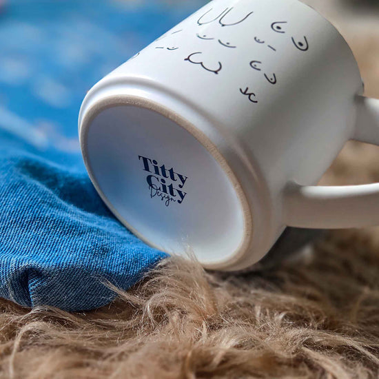 White mug with 'Titty City' branding on a textured surface