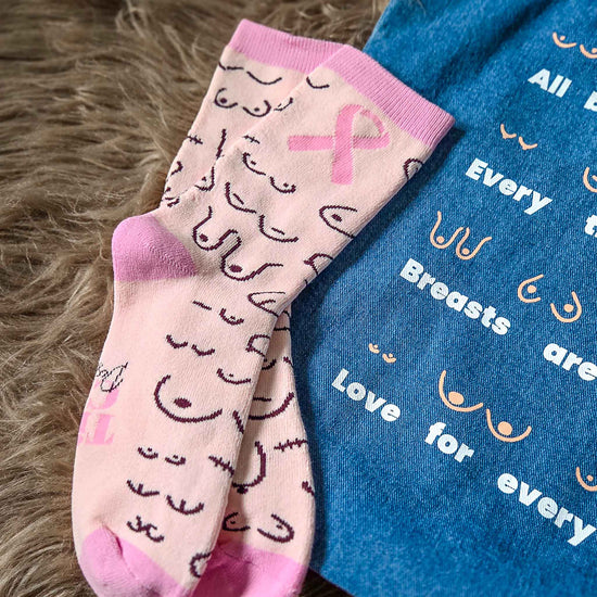 Pink socks with breast cancer awareness symbols and a blue bag with text on a textured surface.