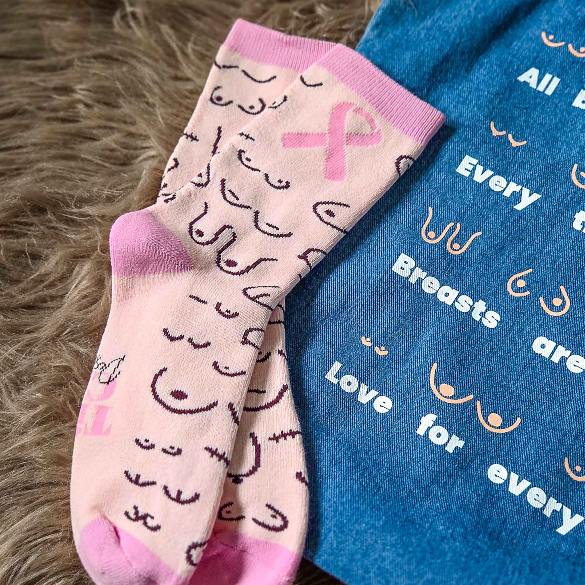 Pink socks with breast cancer awareness symbols and a blue bag with text on a textured surface.