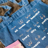 Blue denim tote bag with text and designs on a textured surface