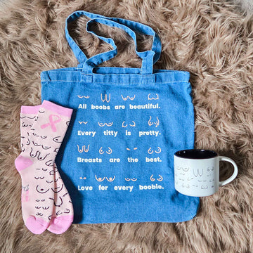 Denim tote bag with text, pink ribbob socks for breast cancer awareness, and white mastectomy mug on a fluffy brown surface