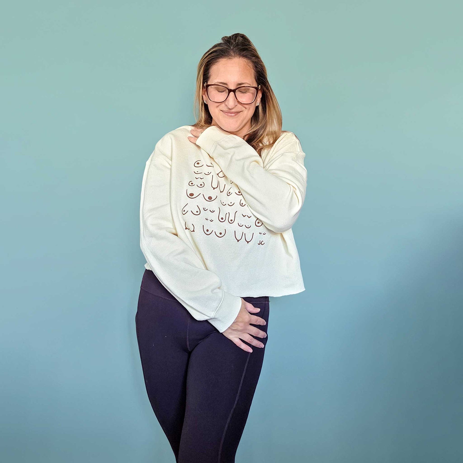 Woman wearing a cream sweatshirt with a body positive graphic design against a blue background