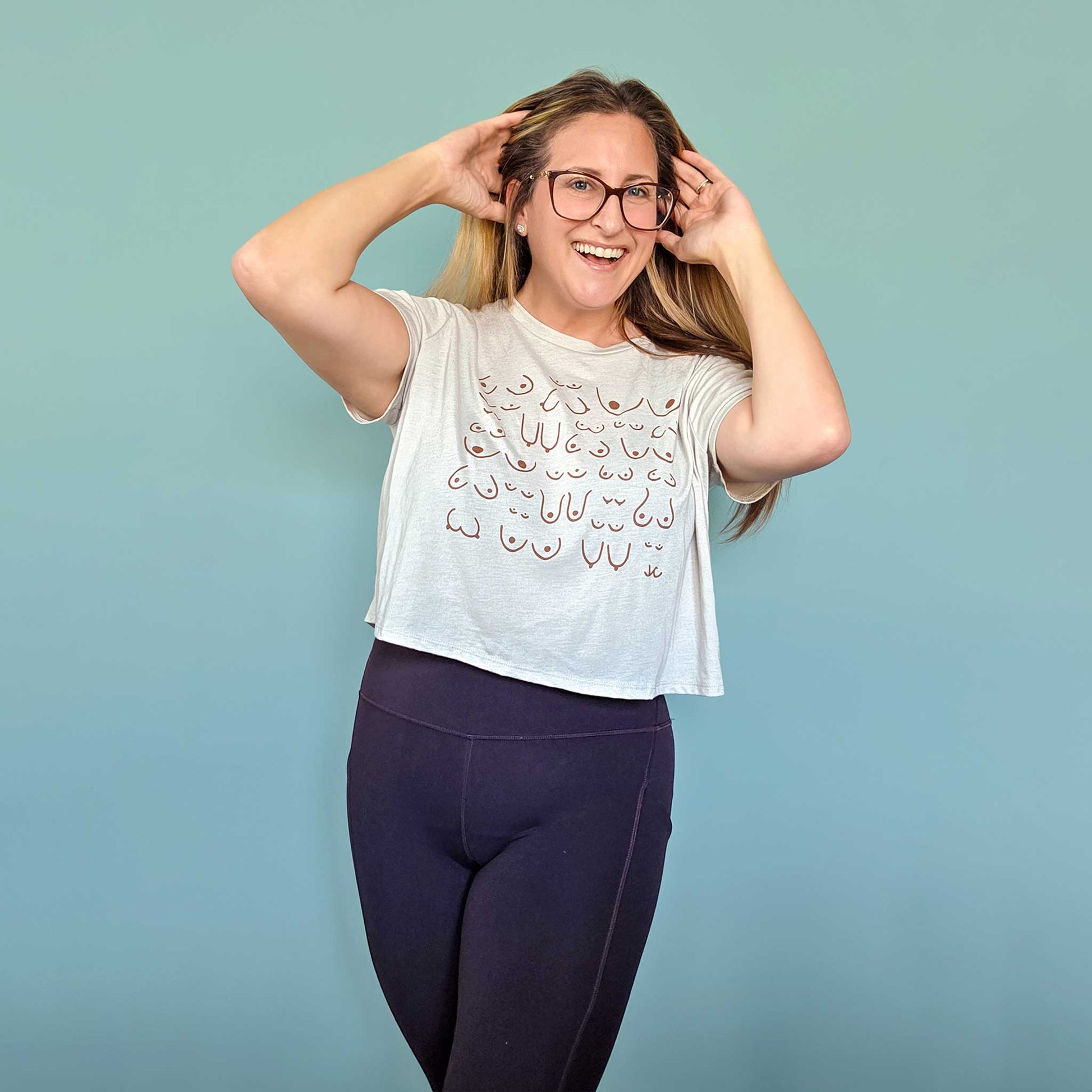 Woman wearing a white crop top with decorative patterns and dark purple leggings against a light blue background
