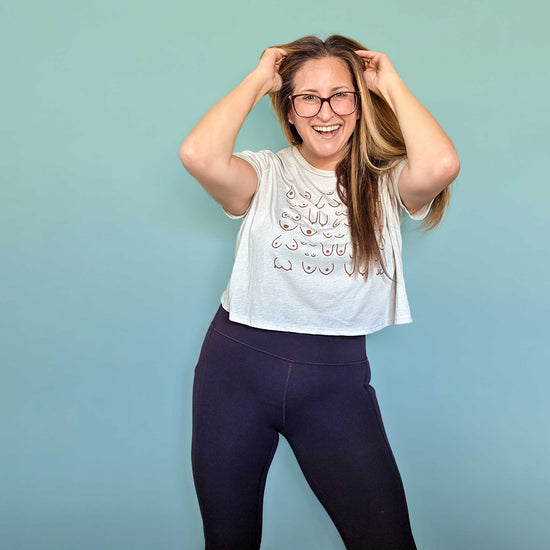 Woman wearing a white t-shirt with a design and dark pants against a light blue background