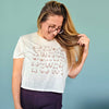 Woman wearing a white t-shirt with a pattern, holding her hair against a blue background