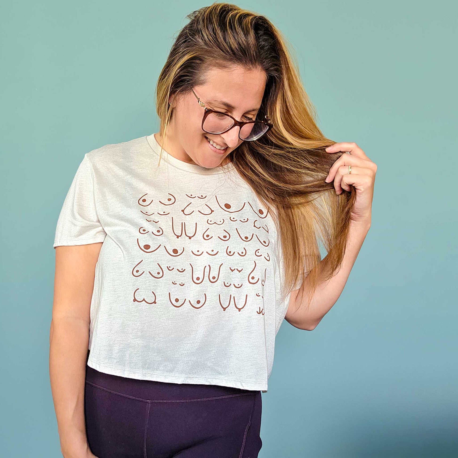 Woman wearing a white t-shirt with a pattern, holding her hair against a blue background
