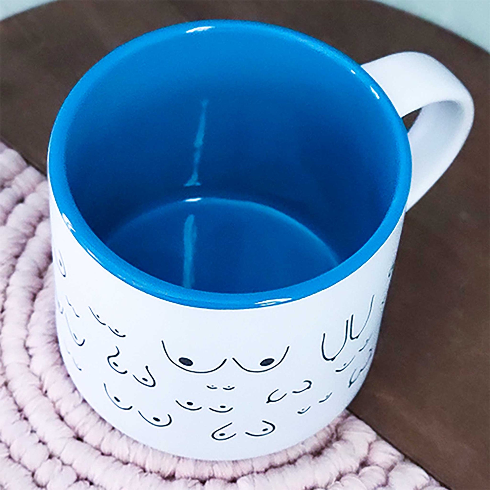White mug with blue interior and rim, featuring a fish scale pattern, on a pink textured surface.