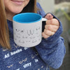 Person holding a mug with a blue interior and black text design, wearing a blue sweater with printed text.
