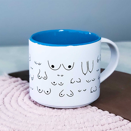 White mug with black line art design on a blue interior, placed on a textured surface.