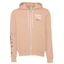 Load image into Gallery viewer, Titty City brand zip-up hooded sweatshirt in peach with logo on left chest and slogan on right sleeve, front view

