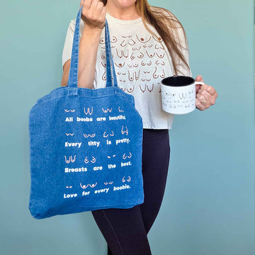 Person holding a blue tote bag with text and a white mug against a light blue background