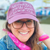 Woman wearing a pink cap and scarf with white text, smiling outdoors.