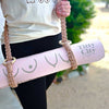Person holding a pink yoga mat with 'Titty City Design' branding, wearing a white shirt and black leggings.
