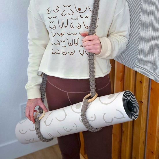 Person holding a yoga mat with a strap against a wooden wall.