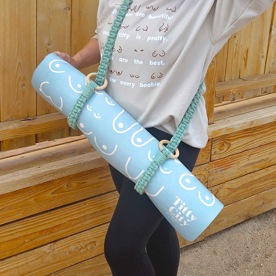 Person holding a light blue yoga mat with white text and design, against a wooden background.